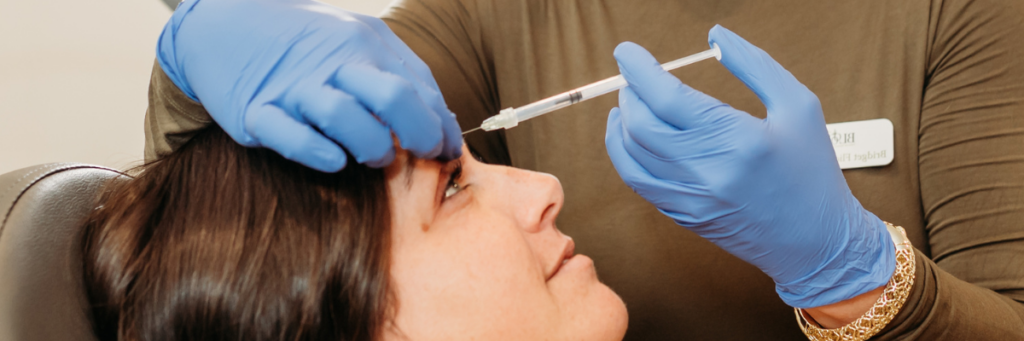 A close up of a woman getting botox between her eyebrows by a doctor wearing blue gloves