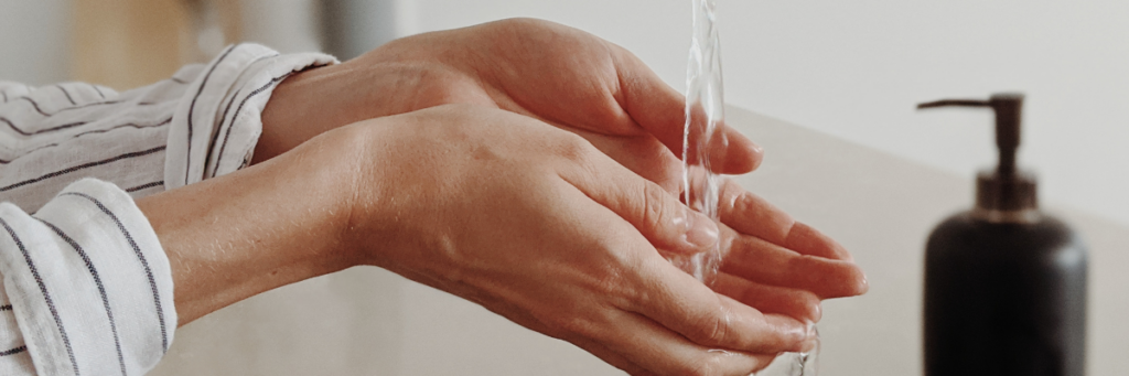 Close up of a woman washing her hands with water running on her hands and the soap bottle beside her