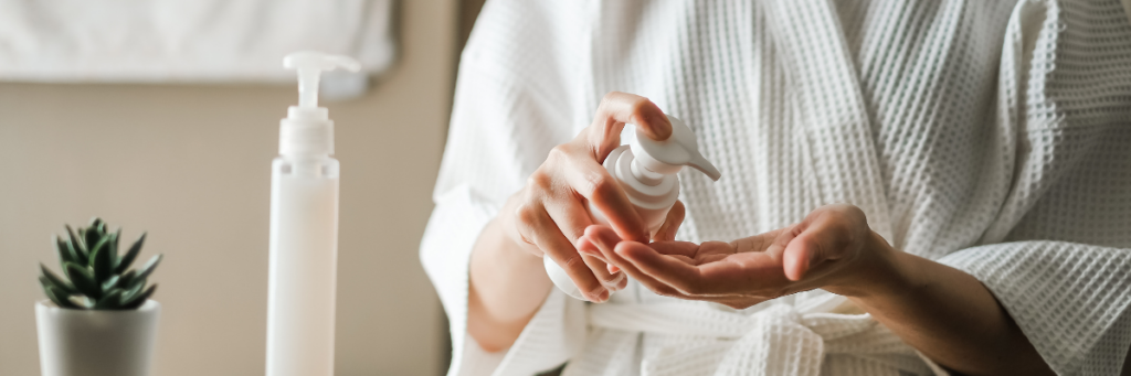 Close up of a woman in a white terry bathrobe pumping lotion into her hand for her skincare routine