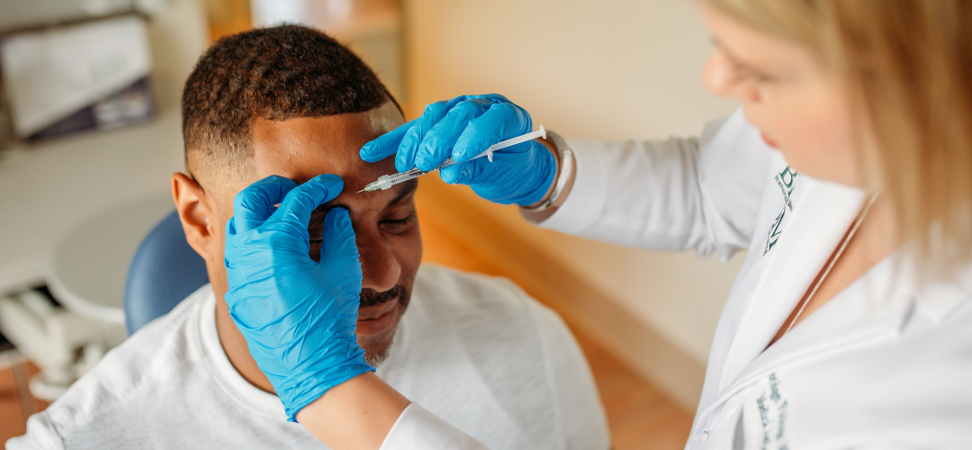 Man receiving botox aesthetic treatment on his forehead by a female technician wearing blue medical gloves and a white coat