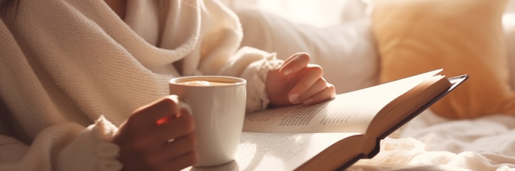 Close up of a woman's torso sitting on a couch holding a cup of coffee and reading a book