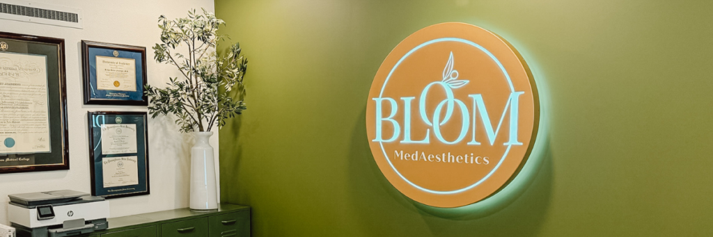 Bloom MedAesthetics logo on a green wall with awards and certifications on a white side wall