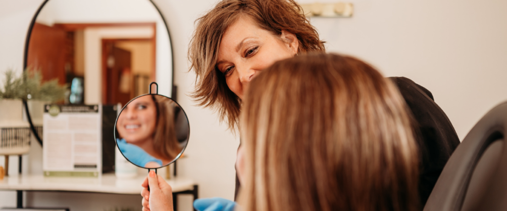 Bloom employee with a client looking in a mirror at her face.