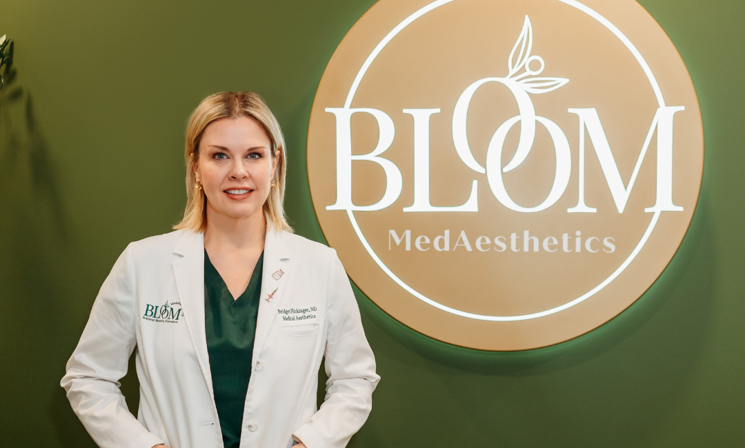 A MedAesthetic Doctor At Her Business Wearing a White Coat Posing In Front of the Bloom MedAesthetic Sign and thinking about prepping your skin for summer