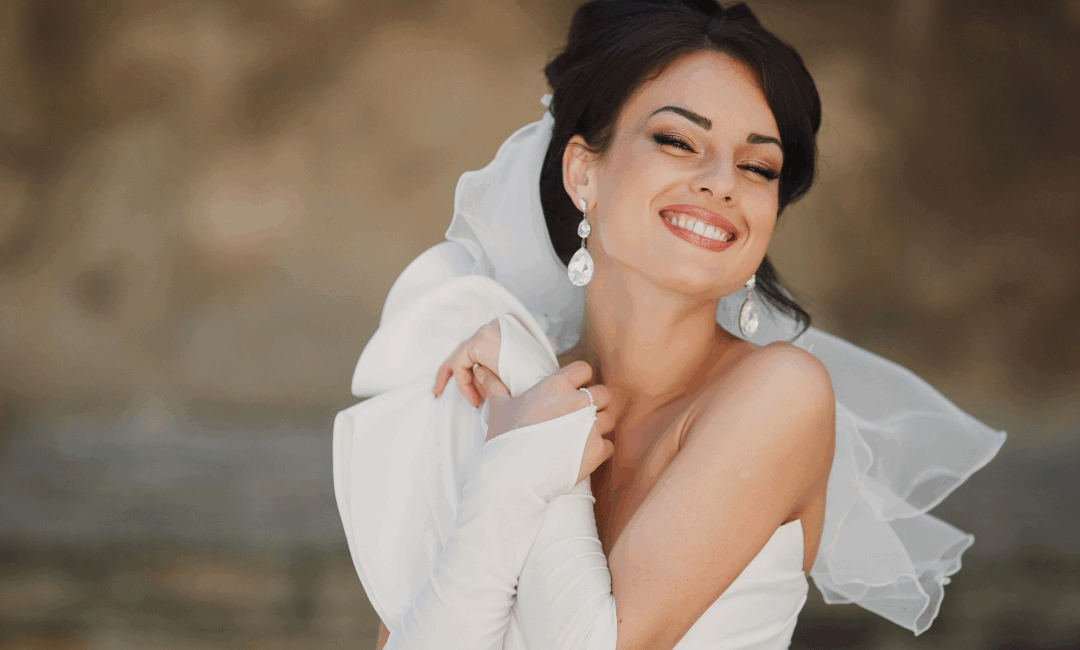 A close up of a woman's upper body and head in a wedding dress with eye closed and smiling after having glowing skin from her pre-wedding aesthetic treatments