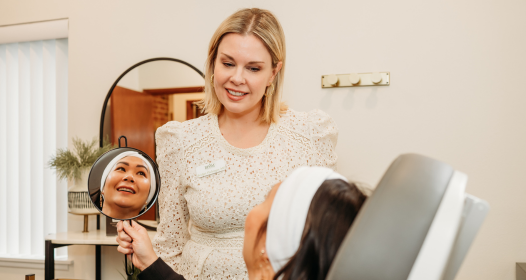 Woman looking in the mirror smiling after receiving skincare services from Bloom